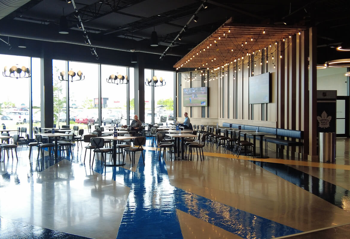 Cineplex junxion polished concrete dining area with tables, people eating, structure with string lights and large windows.